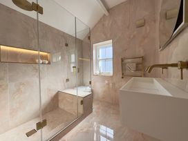 A bathroom with a glass shower enclosure a white sink with a gold faucet a window and beige tiled walls at Ivy House in Conwy