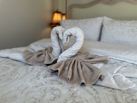Towels folded into two swan shapes forming a heart on a bed with patterned bedspread and pillows at Ivy House in Conwy