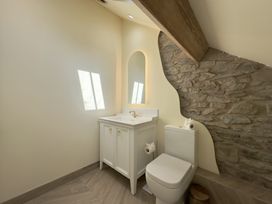 A bathroom with a white vanity sink, a toilet, and a stone accent wall at Ivy House in Conwy