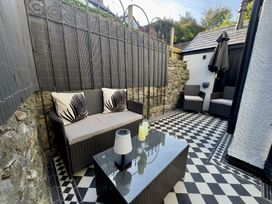 An outdoor patio area with wicker seating and a glass top table on a black and white tiled floor at Ivy House in Conwy