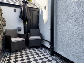 A small outdoor patio with two wicker chairs cushions an umbrella and checkered tile flooring at Ivy House in Conwy