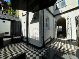An outdoor patio with black and white checkered floor tiles two chairs a glass table an open double door leading inside and a black umbrella at Ivy House Conwy