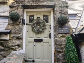 A front door with a wreath and hanging plants on stone walls at Top Cottage in Barmouth