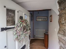 An open white door with a wreath showing a small entryway with a radiator a wooden cabinet and framed pictures at Top Cottage in Barmouth