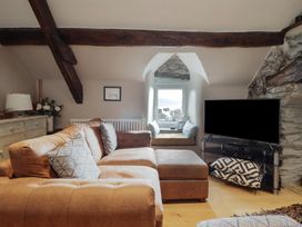 A living room with a brown sofa a small window seat and a television on a stand at Top Cottage in Barmouth