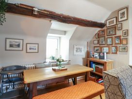 A dining area with a wooden table bench chairs framed pictures on walls and fishing rods on a beam at Top Cottage in Barmouth