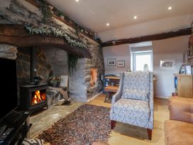 A living room with a burning wood stove a patterned armchair a brown rug and a dining table at Top Cottage in Barmouth