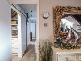 A hallway with light wooden flooring and white walls leading to another room and a dresser with a mirror with driftwood frame and decorative sculptures at Top Cottage in Barmouth