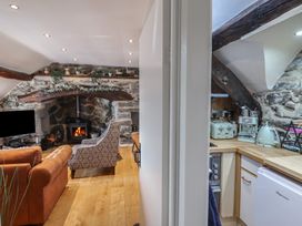 A living room with a fireplace and armchairs next to a kitchen with appliances at Top Cottage in Barmouth