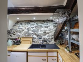 A kitchen with a black sink wooden countertop stone wall and a metal shelf with dishes at Top Cottage in Barmouth