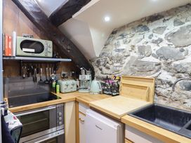 A small kitchen area with wood countertops an electric stove oven a microwave toaster kettle coffee machine and stone wall at Top Cottage in Barmouth