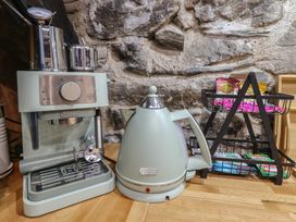A coffee machine kettle and a metal rack with tea bags on a wooden countertop against a stone wall at Top Cottage in Barmouth