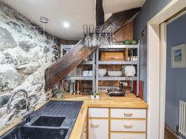 A kitchen corner with a black sink wooden countertop open metal shelves with dishes and glassware at Top Cottage in Barmouth