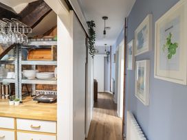 A hallway with blue walls and framed pictures alongside a kitchen counter with dishes and glasses at Top Cottage in Barmouth