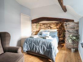 A bedroom with a bed with blue bedding under a wooden beam and stone wall next to a door and an armchair with a plant in a pot at Top Cottage in Barmouth