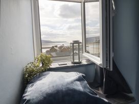 A window with an open white frame a gray cushion a small plant and a lantern on the windowsill at Top Cottage in Barmouth