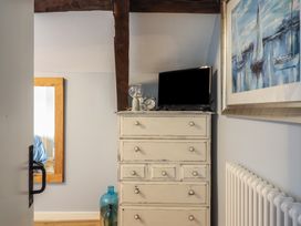 A chest of drawers with a TV clock and lamp on top in a room with a radiator and a painting of sailboats at Top Cottage in Barmouth