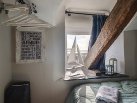 A bedroom corner with hanging clothes hangers a framed print a model sailboat on the windowsill and two lanterns at Top Cottage in Barmouth