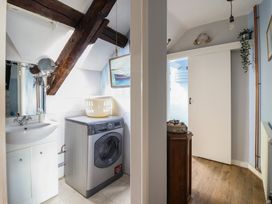 A laundry room with a washing machine and sink next to a hallway with a white sliding door at Top Cottage in Barmouth