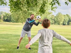 A person playing catch with a child using a soccer ball in a park at Ripples & Reeds - Billing Aquadrome