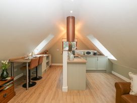 A kitchen with a central island under sloped ceilings with two brown bar stools and a brown leather armchair at Pheasants Rise Apartment in Ross-On-Wye