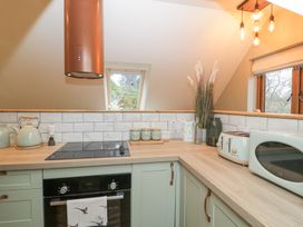 A kitchen with light green cabinets a black oven an electric stove a kettle toaster microwave and a window at Pheasants Rise Apartment in Ross-On-Wye