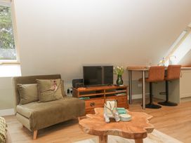 A living area with an olive green sofa and bird cushion a wooden TV stand with a flat screen TV a wooden coffee table with candles and coasters and a dining counter with two brown chairs at Pheasants Rise Apartment in Ross-On-Wye