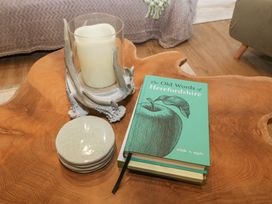 A wooden coffee table with a book called The Old Words of Herefordshire a candle in a glass holder with antler design and a stack of coasters in a living room at Pheasants Rise Apartment in Ross-On-Wye
