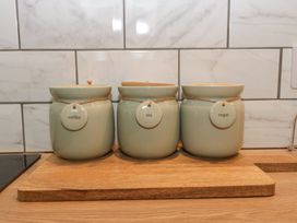 Three labeled containers for coffee tea and sugar on a wooden board in a kitchen at Pheasants Rise Apartment in Ross-On-Wye