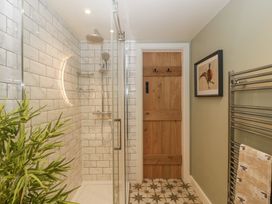 A bathroom with a glass shower enclosure wooden door wall art plant and patterned tile floor at Pheasants Rise Apartment in Ross-On-Wye