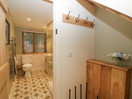 A bathroom with a toilet, shower enclosure, window with blinds, and a wooden cabinet with a flower vase at Pheasants Rise Apartment in Ross-On-Wye
