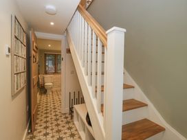 A hallway with wooden stairs and patterned tiled floor leading to a bathroom with a toilet and window at Pheasants Rise Apartment Ross-On-Wye