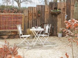 A small outdoor seating area with two white metal chairs and a table on a gravel surface surrounded by wooden fencing