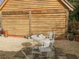 A patio with a white metal table and two chairs beside a wooden shed and potted plants at Pheasants Rise Apartment in Ross-On-Wye