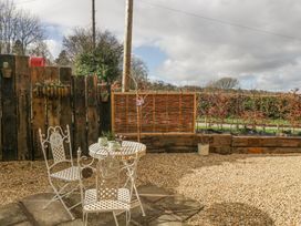 A small outdoor seating area with two metal chairs and a round table on a gravel surface near wooden fencing and plants at Pheasants Rise Apartment in Ross-On-Wye