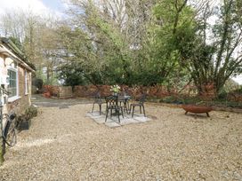 An outdoor patio area with a metal table and chairs set on stone tiles surrounded by gravel and trees at Pheasants Rise Apartment in Ross-On-Wye