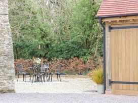 An outdoor seating area with a metal table and chairs on gravel next to a wooden door and stone wall surrounded by trees