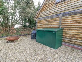 An outdoor area with a fire pit a covered grill a green storage box and a wooden wall with plants in the background at Pheasants Rise Apartment in Ross-On-Wye