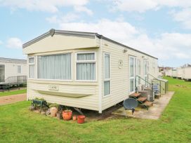 A beige caravan with steps and potted plants on a grass lawn at 120 Caravan in Hemsby
