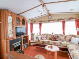 A living room with a floral sofa a wooden cabinet with a television and a fireplace at 120 Caravan in Hemsby