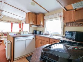 A kitchen area with wooden cabinets a sink a microwave and an appliance on the counter at 120 Caravan in Hemsby