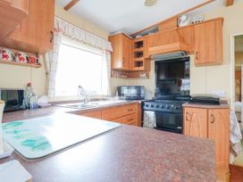 A kitchen with wooden cabinets a black stove microwave and a sink under a window at 120 Caravan in Hemsby