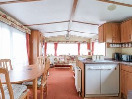 An open-plan living area with a wooden dining table and chairs a kitchenette with appliances and cabinets and a sofa with floral cushions at 120 Caravan in Hemsby