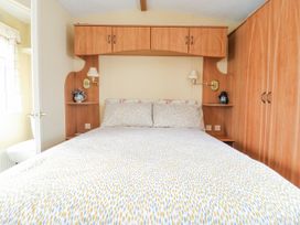 A bedroom with a bed, overhead cabinets, bedside shelves, wall lamps, and a wardrobe at 120 Caravan in Hemsby