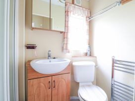 A bathroom with a sink, toilet, mirrored cabinet, window with checked curtain and a towel rack at 120 Caravan in Hemsby