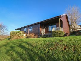 A single story wooden lodge with steps and shrubs on a grassy hill under a clear blue sky at Creag Mhor Lodge Back of Keppoch near Arisaig