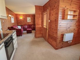A living area with wooden walls red sofas a kitchen counter an oven and a wooden door at Creag Mhor Lodge Back of Keppoch near Arisaig
