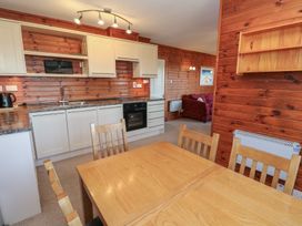 A kitchen and dining area with wooden chairs and table white cabinets and wood panel walls at Creag Mhor Lodge Back of Keppoch near Arisaig