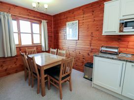A dining area with a wooden table and six chairs next to a window with curtains in a room with wood-paneled walls at Creag Mhor Lodge Back of Keppoch near Arisaig