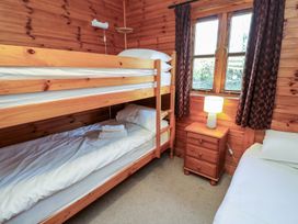 A bedroom with wooden bunk beds a single bed a wooden nightstand with a lamp and a window with curtains at Creag Mhor Lodge Back of Keppoch near Arisaig